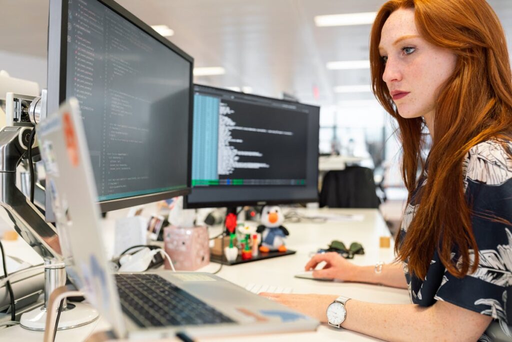 Female engineer working on complex software across three monitors and two computers