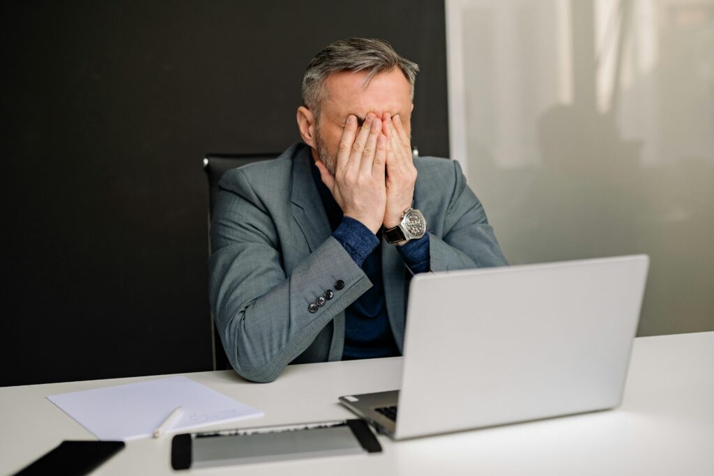 Businessman at laptop covering his face in frustration